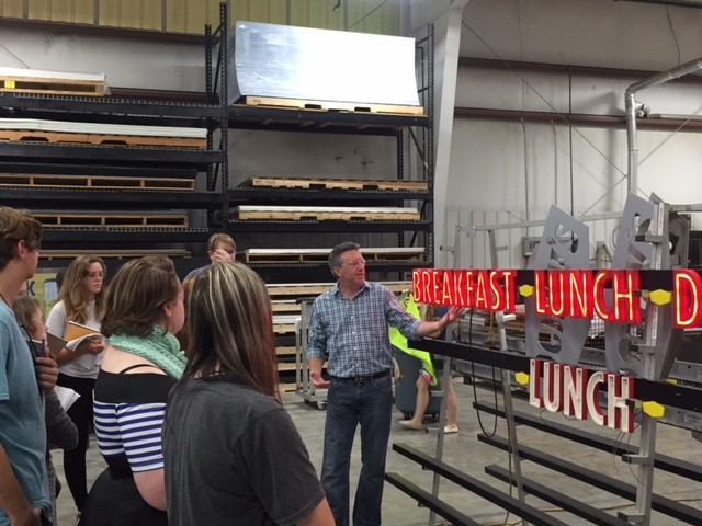 A man showing the neon signs to a group of people
